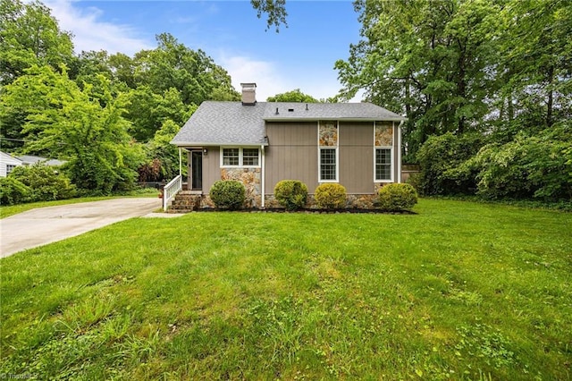 view of front of home with a chimney, a front lawn, concrete driveway, and stone siding