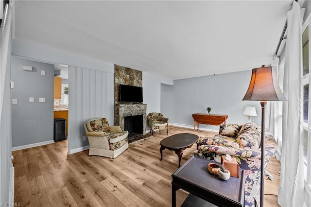 living room featuring light wood finished floors, a stone fireplace, and baseboards