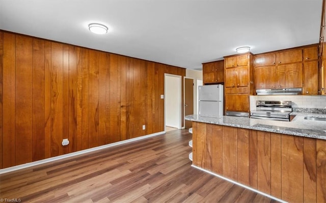 kitchen with hardwood / wood-style floors, light stone counters, white refrigerator, and stainless steel range with electric stovetop