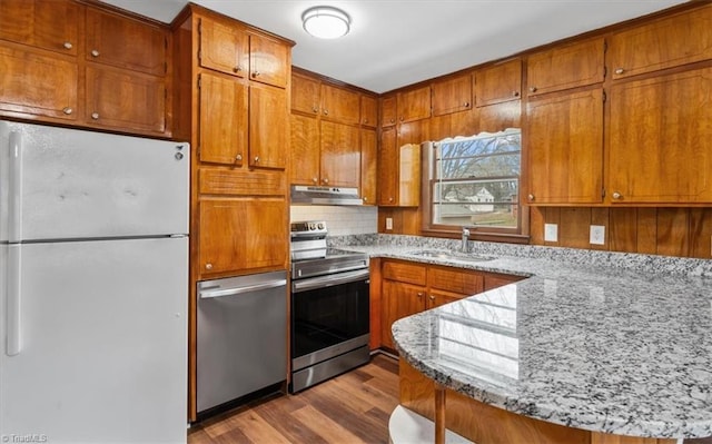 kitchen with light hardwood / wood-style floors, kitchen peninsula, sink, light stone countertops, and appliances with stainless steel finishes