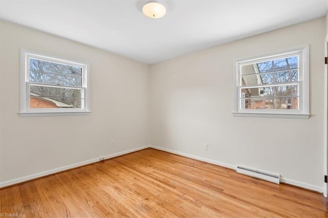 unfurnished room with baseboard heating, a wealth of natural light, and light wood-type flooring