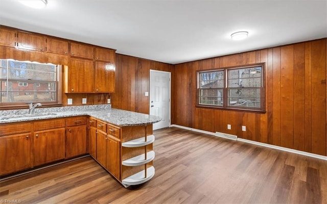 kitchen with light stone countertops, wooden walls, sink, kitchen peninsula, and hardwood / wood-style flooring