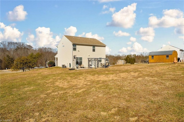 rear view of property featuring a yard, central AC unit, and a storage unit