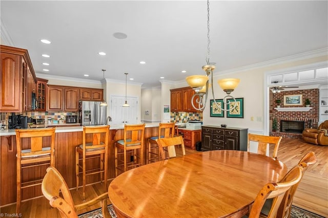 dining room with crown molding, a fireplace, a ceiling fan, recessed lighting, and light wood finished floors