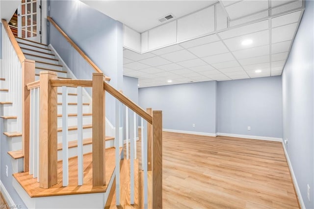 staircase featuring visible vents, baseboards, a paneled ceiling, and wood finished floors