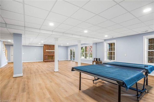 rec room featuring baseboards, light wood-type flooring, a paneled ceiling, and decorative columns