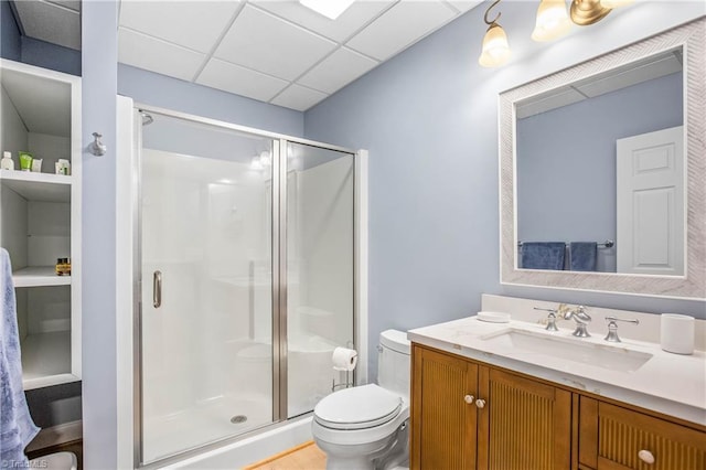 full bathroom featuring a shower stall, vanity, a drop ceiling, and toilet