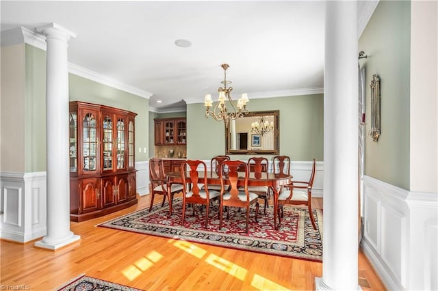 dining area featuring ornate columns, wood finished floors, ornamental molding, and a wainscoted wall