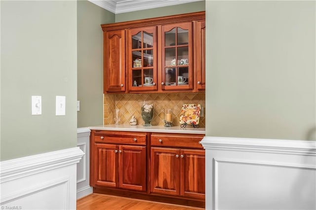 bar with tasteful backsplash, light wood finished floors, and crown molding