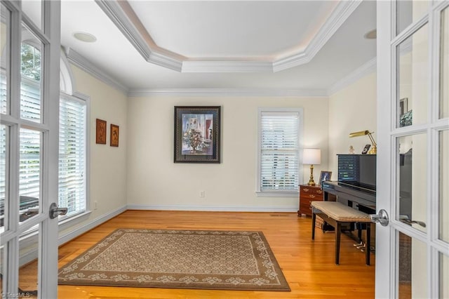 interior space with baseboards, french doors, crown molding, a raised ceiling, and wood finished floors