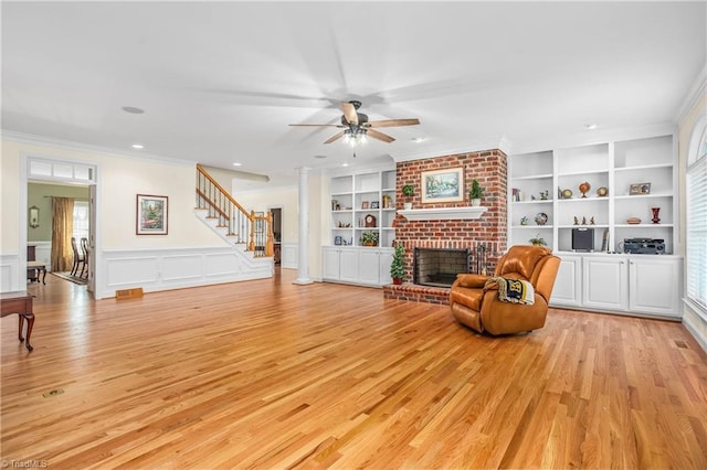 living area with built in shelves, ceiling fan, light wood-type flooring, a fireplace, and crown molding
