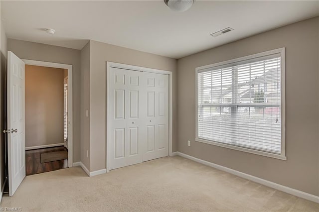 unfurnished bedroom featuring baseboards, light carpet, a closet, and visible vents