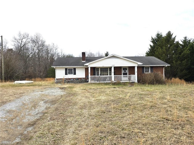 view of front of home with brick siding, a chimney, covered porch, driveway, and a front lawn