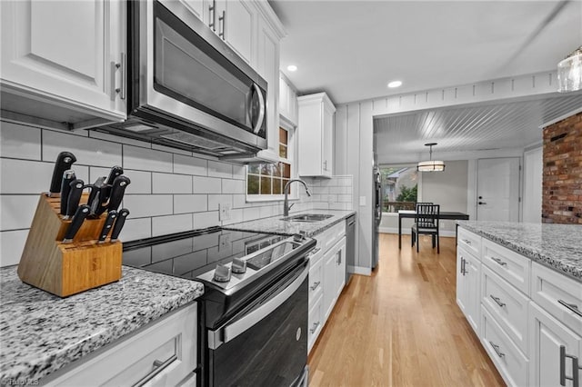 kitchen with white cabinets, a sink, appliances with stainless steel finishes, light wood finished floors, and backsplash