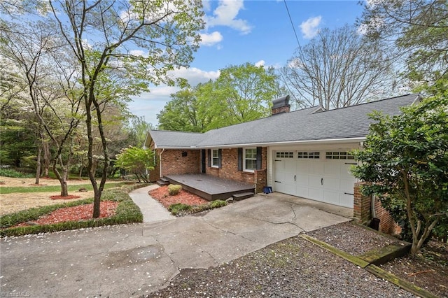 ranch-style home featuring a shingled roof, an attached garage, a chimney, brick siding, and driveway