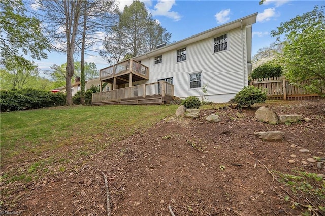 rear view of house featuring fence, a deck, and a lawn