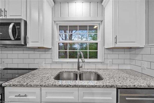kitchen with light stone countertops, tasteful backsplash, white cabinetry, appliances with stainless steel finishes, and a sink