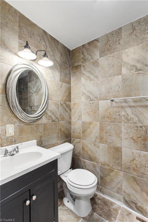 bathroom featuring vanity, tile walls, and toilet