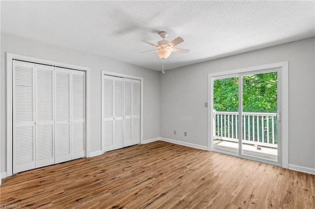 unfurnished bedroom featuring access to outside, wood finished floors, multiple closets, baseboards, and a textured ceiling