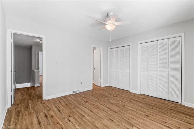 unfurnished bedroom with baseboards, two closets, light wood-style floors, and ceiling fan