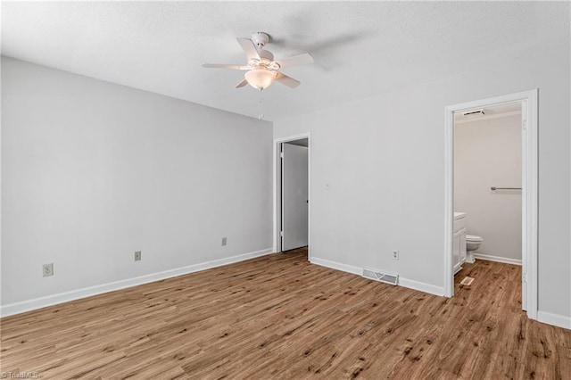 unfurnished bedroom featuring wood finished floors, ensuite bath, baseboards, and ceiling fan