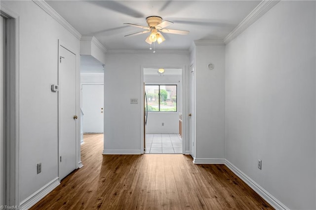 spare room featuring ceiling fan, wood finished floors, baseboards, and crown molding