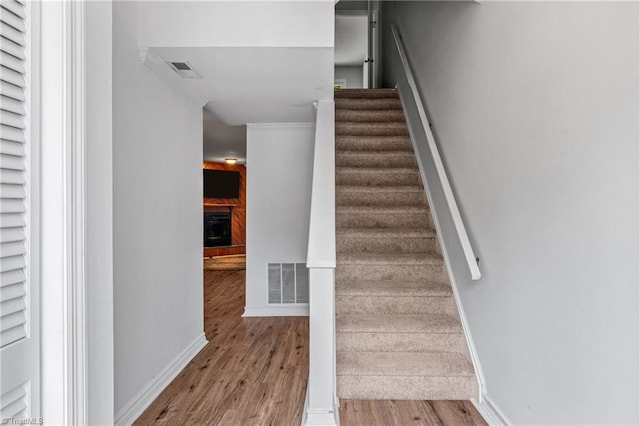 stairs featuring wood finished floors, a fireplace, baseboards, and ornamental molding
