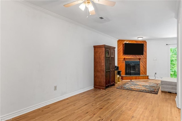unfurnished living room with a large fireplace, light wood-style flooring, crown molding, ceiling fan, and baseboards