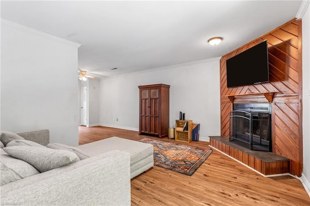 living area with crown molding, a brick fireplace, light wood-style flooring, ceiling fan, and baseboards
