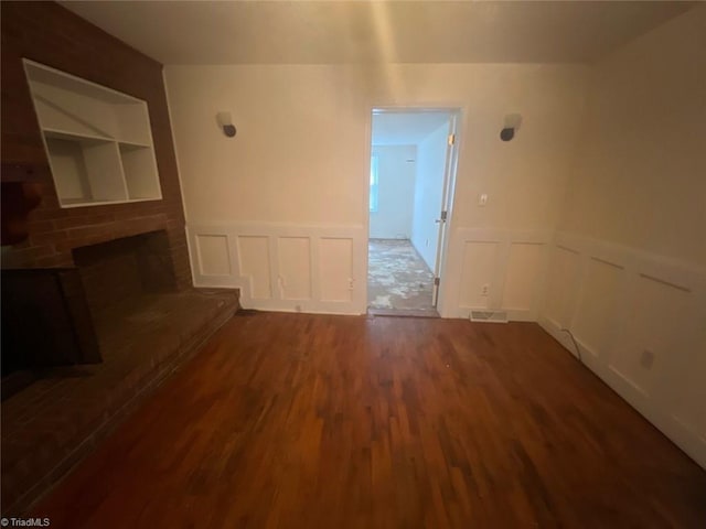 spare room with a brick fireplace and dark hardwood / wood-style floors