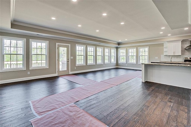 unfurnished living room featuring a tray ceiling, baseboards, ornamental molding, and dark wood-style flooring