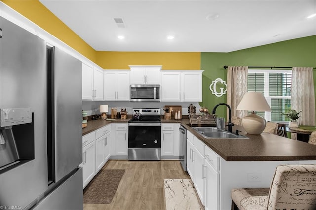 1009 Cannonade Dr, Whitsett, NC 27377 - kitchen featuring stainless steel appliances, a sink, a peninsula, dark countertops, and white cabinetry