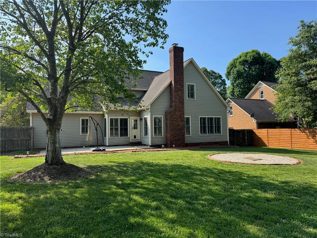 rear view of property with fence, a chimney, a yard, and a patio area