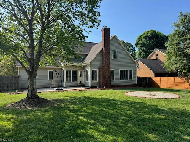 rear view of property with fence, a chimney, a yard, and a patio area