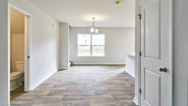 unfurnished dining area with an inviting chandelier, wood finished floors, and baseboards