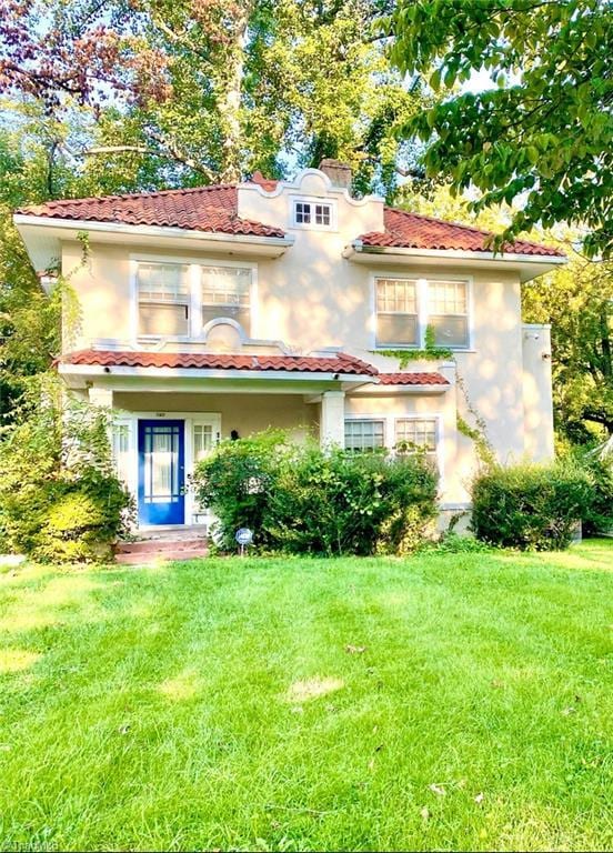 mediterranean / spanish-style home with a front yard, a tiled roof, and stucco siding