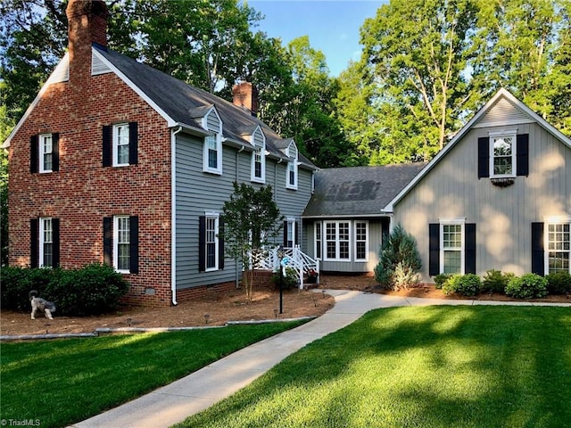 view of front of home with a shingled roof, a chimney, crawl space, a front lawn, and brick siding