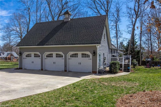 view of side of home featuring a shingled roof, a detached garage, a deck, and a lawn