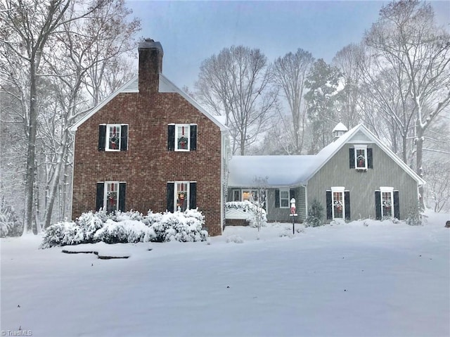 snow covered property with a chimney and brick siding