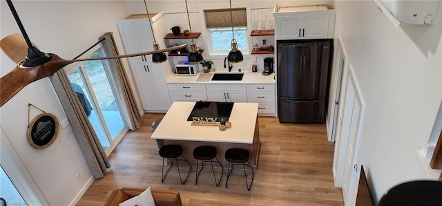 kitchen with white cabinetry, light hardwood / wood-style floors, black refrigerator, pendant lighting, and sink