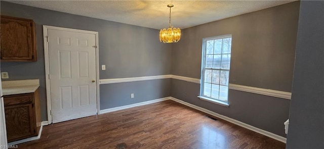 unfurnished dining area featuring dark hardwood / wood-style flooring, a textured ceiling, and a notable chandelier