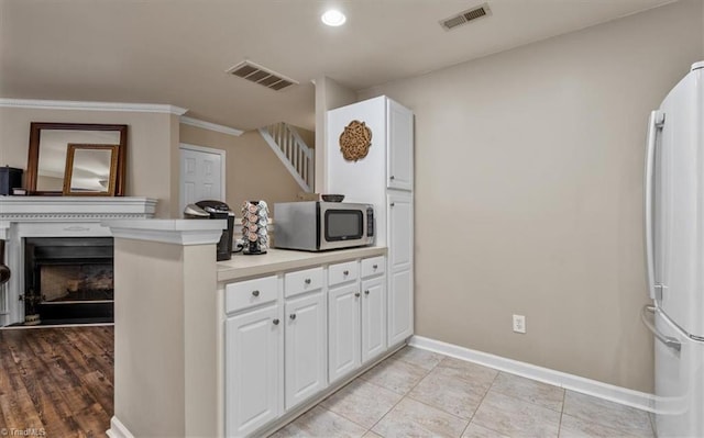 kitchen featuring visible vents, stainless steel microwave, freestanding refrigerator, and white cabinets