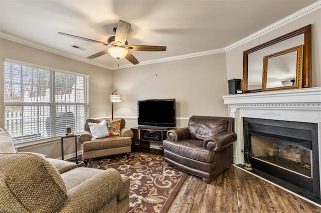 living room with visible vents, a ceiling fan, a glass covered fireplace, ornamental molding, and wood finished floors