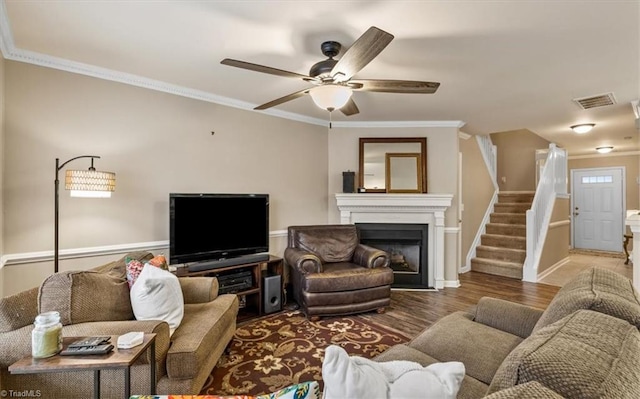 living room with crown molding, visible vents, ceiling fan, wood finished floors, and stairs