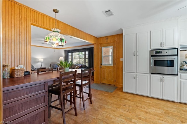 kitchen with pendant lighting, white cabinetry, oven, and wooden walls