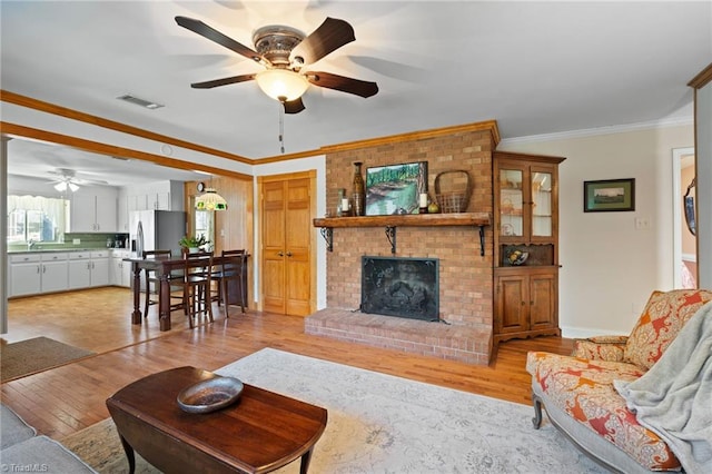 living room featuring a fireplace, sink, crown molding, and light hardwood / wood-style flooring