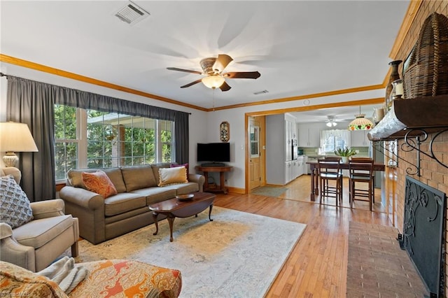 living room featuring crown molding, light hardwood / wood-style flooring, ceiling fan, and a brick fireplace