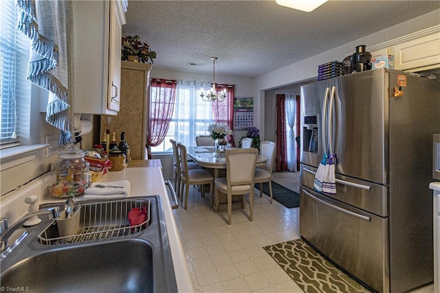 kitchen featuring stainless steel refrigerator with ice dispenser, pendant lighting, sink, a textured ceiling, and an inviting chandelier