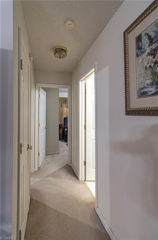 hall featuring light carpet and a textured ceiling