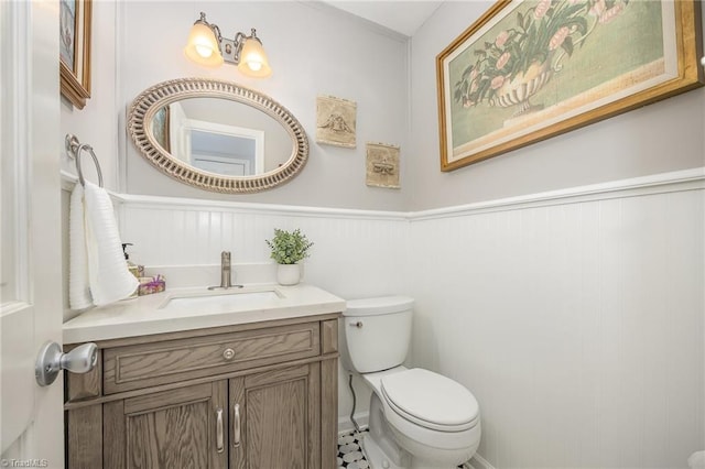 half bathroom with vanity, wainscoting, and toilet